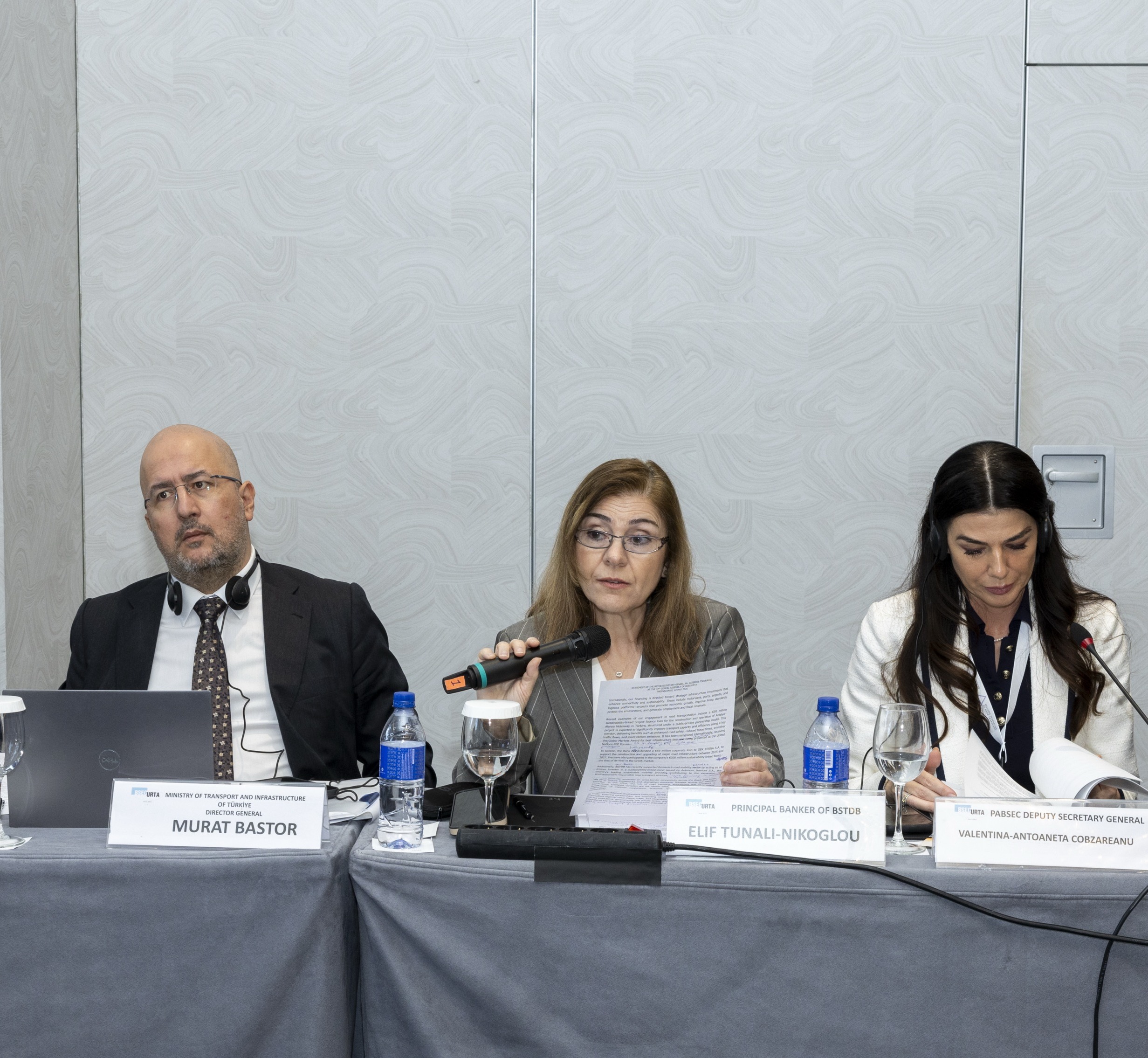 Three panel participants seated at a conference table during the 47th BSEC-URTA General Assembly. Elif Tunali Nikoglou, BSTDB Principal Banker for General Industries, Transport and Tourism 2 (center), delivers remarks during the session.
